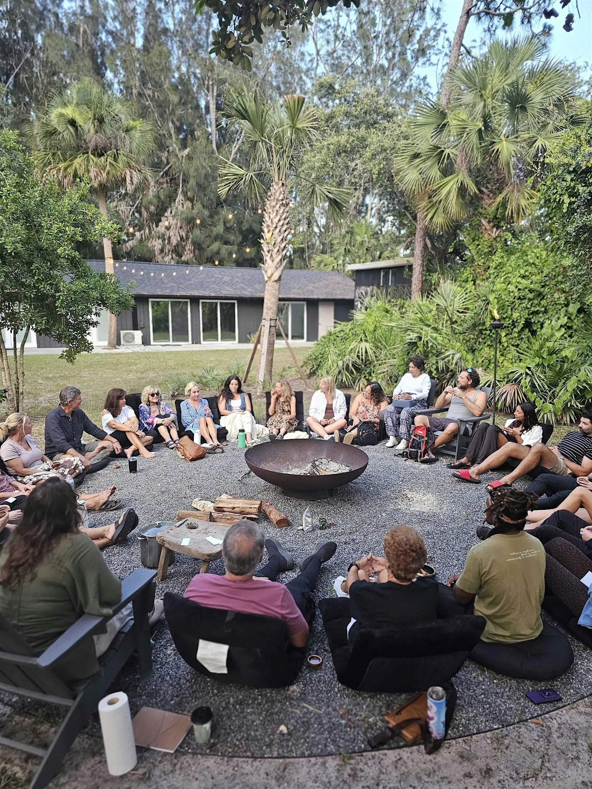 A large informal circle gathered outdoors around a fire pit.